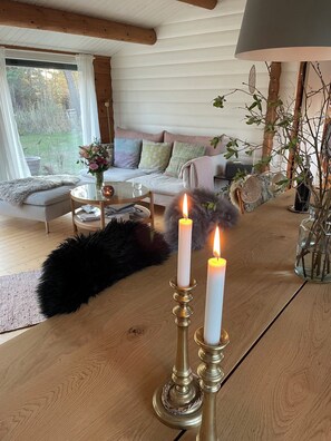 A cozy living room with a wooden table, two lit candles, a sofa, and a view of the outdoors. - Danish summerhouse with Danish Holiday Atmosphere (Væggerløse)