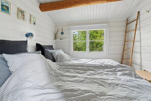 A bedroom with a bed, a window, a ladder, and wall-mounted artwork. - Danish summerhouse with Danish Holiday Atmosphere (Væggerløse)