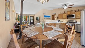 Un coin repas avec une table ronde en bois, des chaises en bois, un lustre et un ventilateur de plafond.