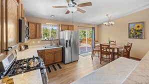 Une cuisine avec des meubles de rangement en bois, un réfrigérateur en acier inoxydable, une cuisinière à gaz et un ventilateur de plafond.