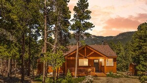 Une cabane dotée d’un porche, entourée d’arbres, avec une montagne en arrière-plan.