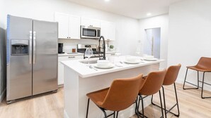 A modern kitchen with white cabinetry, stainless steel appliances, a central island with bar stools, and a dining area. - 2BR Home | Near T | Free Street Parking (Pittsburgh)