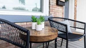 A wooden table with two potted plants, black wicker chairs, and a window with a view of buildings. - 2BR Home | Near T | Free Street Parking (Pittsburgh)