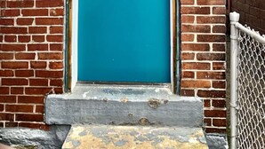 Une porte bleue sur laquelle est écrit « Bonjour ! », une boîte aux lettres et un mur de briques.