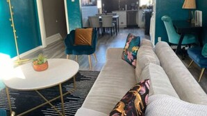 Un salon moderne avec un canapé, des fauteuils, un coin repas et une cuisine en arrière-plan.