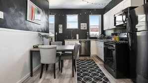 Une cuisine moderne avec un coin repas, comprenant un réfrigérateur noir, des appareils en acier inoxydable et un tapis à motifs.