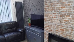 Ein Wohnzimmer mit Kamin aus Ziegelsteinen, einer Ledersofa, einem Fernseher auf einem Schrank und einer Wand mit Muster.