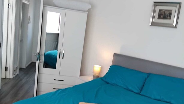Ein Schlafzimmer mit einem Bett, einem Kleiderschrank, einem Nachttisch mit Lampe und einem gerahmten Bild an der Wand.