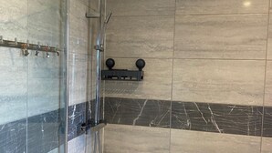 Ein modernes Badezimmer mit einer Duschkabine aus Glas, einer Handbrause und einer eingebauten Ablagefläche mit zwei runden Gegenständen.