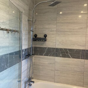 Ein modernes Badezimmer mit einer Duschkabine aus Glas, einer Handbrause und einer eingebauten Ablagefläche mit zwei runden Gegenständen.