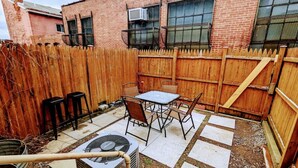 A backyard with a patio, a table with chairs, a wooden fence, and a brick building in the background. - 1 Block from Butler St ★ Patio ★ Dog Friendly! (Pittsburgh)