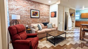 A living room with a brick wall, a red armchair, a beige sofa, and a coffee table. - 1 Block from Butler St ★ Patio ★ Dog Friendly! (Pittsburgh)