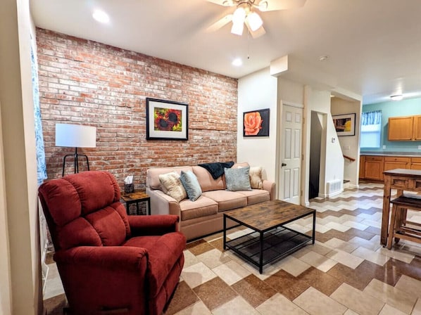 A living room with a brick wall, a red armchair, a beige sofa, and a coffee table.