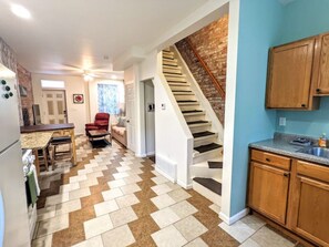 A kitchen with a herringbone floor pattern, wooden cabinets, a red chair, and a staircase with a brick wall.