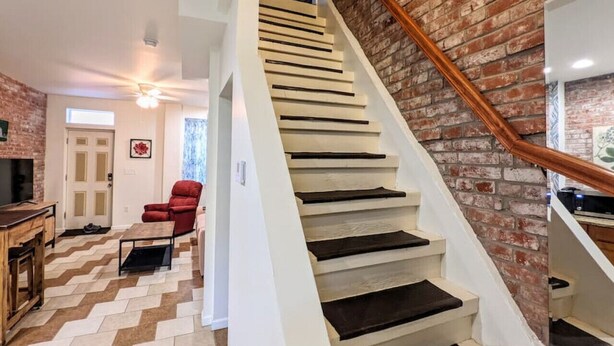 A staircase with a wooden handrail, a brick wall, and a herringbone floor pattern. - 1 Block from Butler St ★ Patio ★ Dog Friendly! (Pittsburgh)