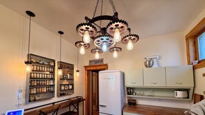 A kitchen with a white refrigerator, wooden bar stools, a hanging light fixture with gears, and a sign that reads 'Pittsburgh'. - NFL Draft Stay "The Little Gallimaufry House" (Pittsburgh)