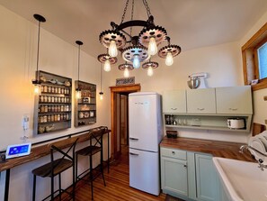 Une cuisine avec un réfrigérateur blanc, des tabourets de bar en bois, un luminaire suspendu orné d’engrenages et un panneau indiquant « Pittsburgh ».