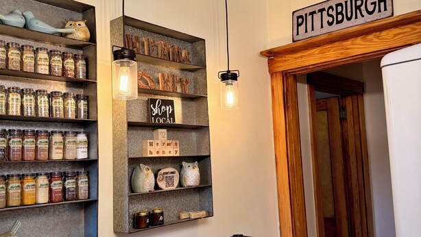A kitchen with wooden shelves holding jars, a sign reading 'Pittsburgh,' and a wooden bar stool. - NFL Draft Stay "The Little Gallimaufry House" (Pittsburgh)