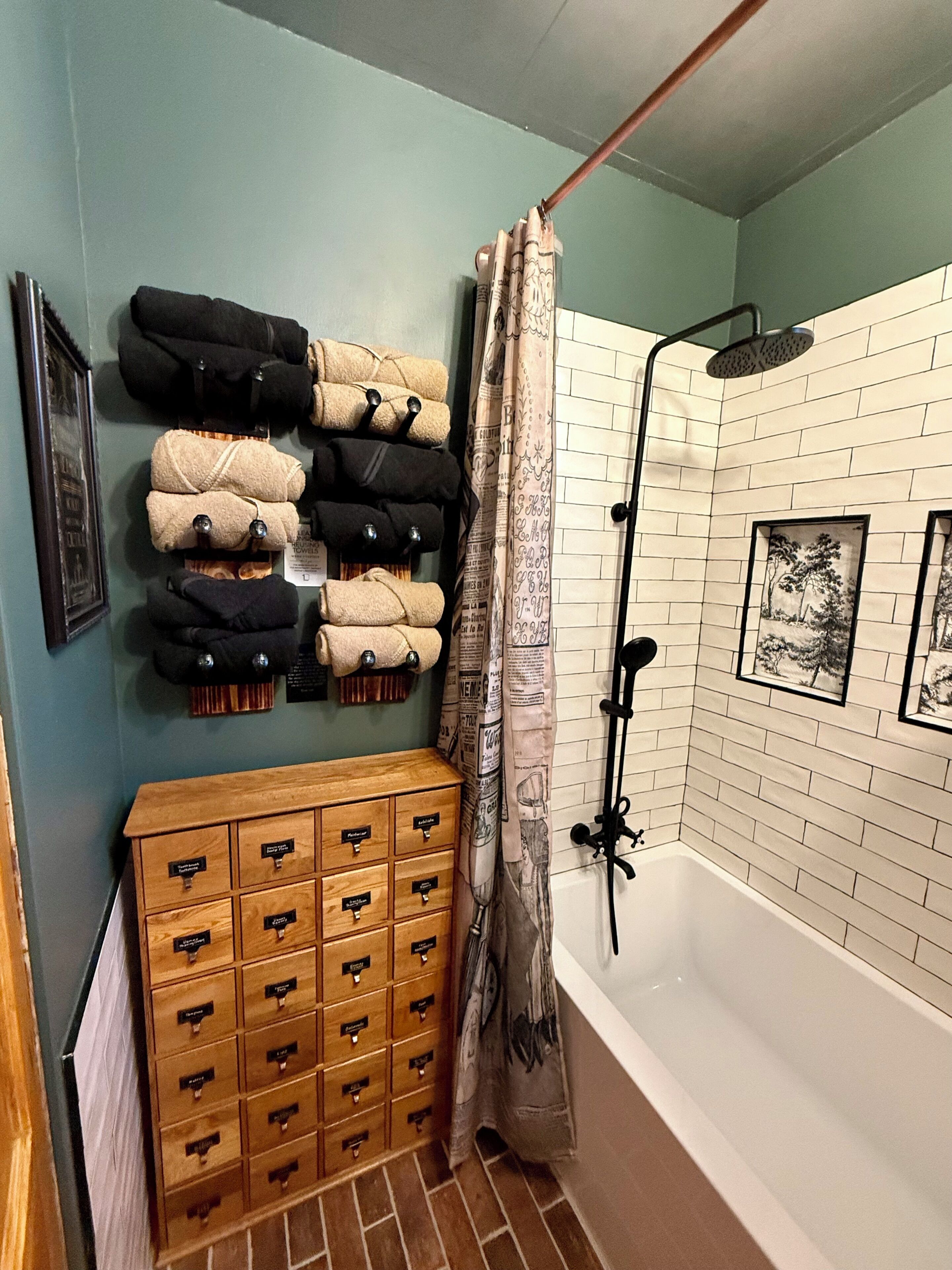 A bathroom with a bathtub, a shower, a towel rack with neatly folded towels, and a wooden storage unit with drawers.