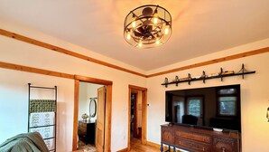 A living room with a wooden floor, a leather sofa, a wooden cabinet with a TV, and a chandelier. - NFL Draft Stay "The Little Gallimaufry House" (Pittsburgh)