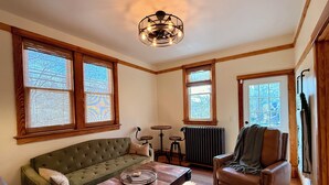 A room with a green sofa, a brown leather chair, a wooden coffee table, and a ceiling light fixture. - NFL Draft Stay "The Little Gallimaufry House" (Pittsburgh)