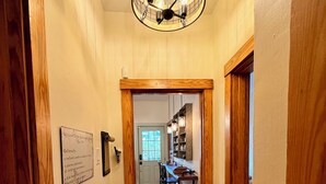 A hallway with wooden flooring, a bench, a chandelier, and a kitchen area with bar stools. - NFL Draft Stay "The Little Gallimaufry House" (Pittsburgh)