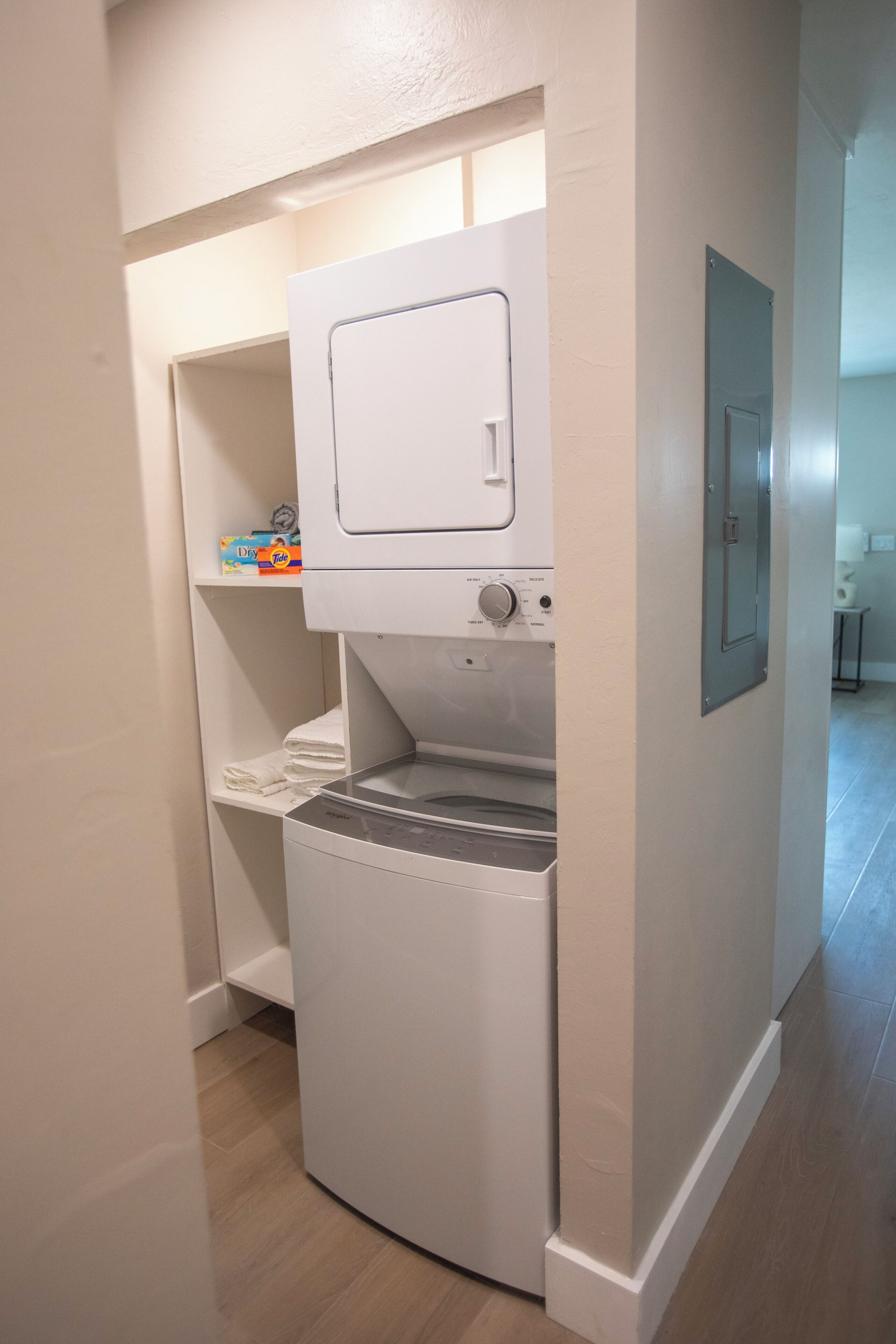 A compact laundry room with a washing machine, a dryer, and a shelf with laundry supplies.