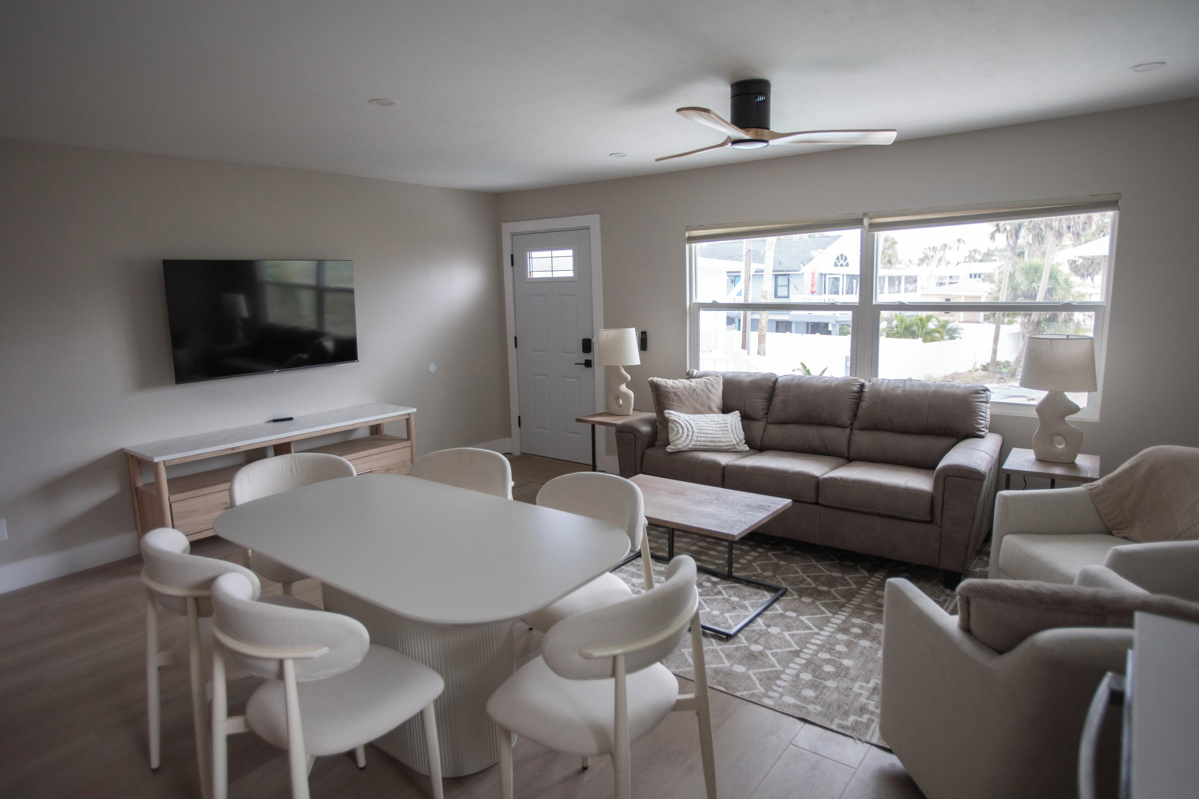 A modern living room with a dining table, chairs, a sofa, a TV, and a ceiling fan.