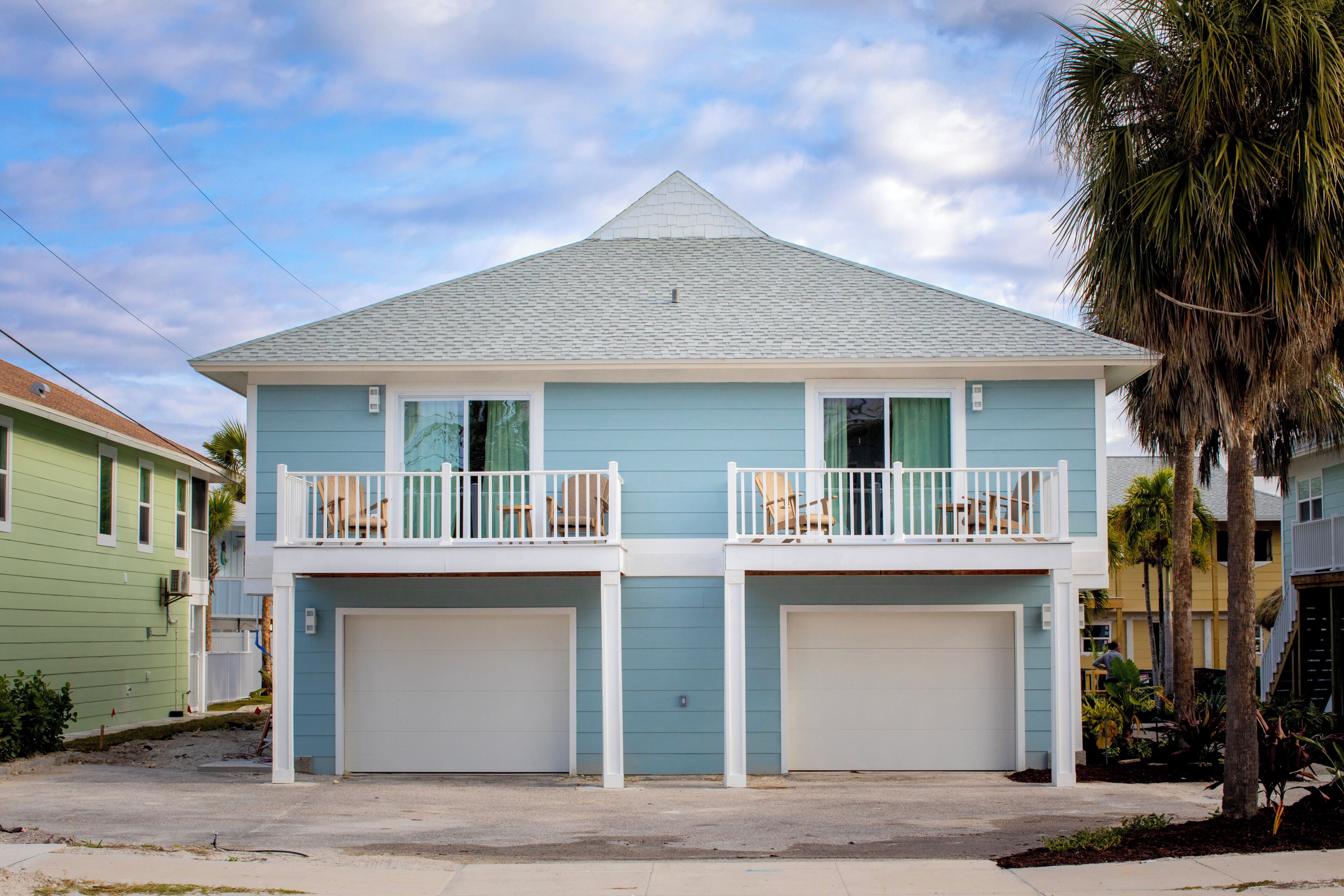 A two-story house with a garage, a balcony on the upper floor, and a palm tree in the foreground.
