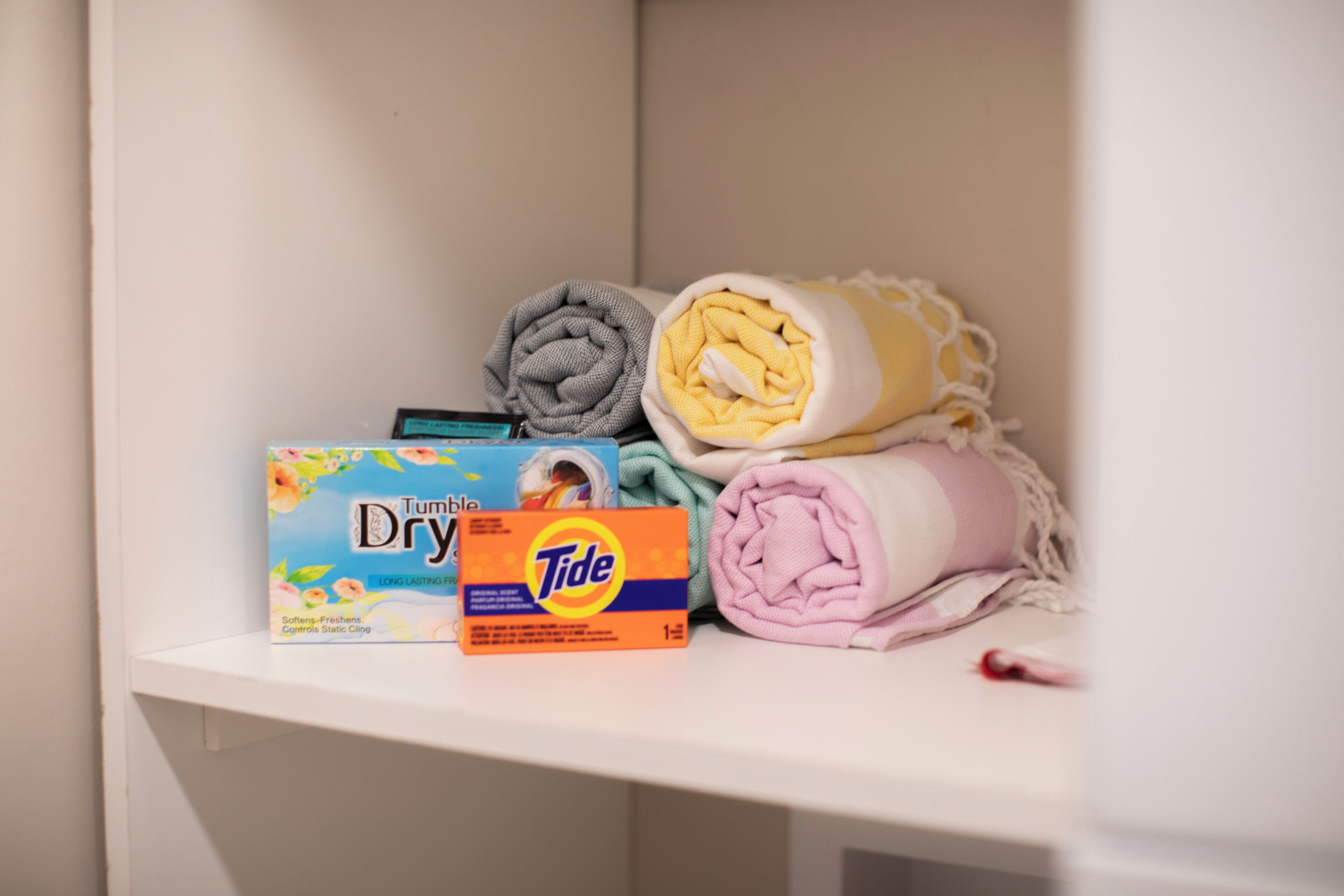 Un estante con ropa doblada, una caja de detergente Tide y una caja de Tumble Dry.