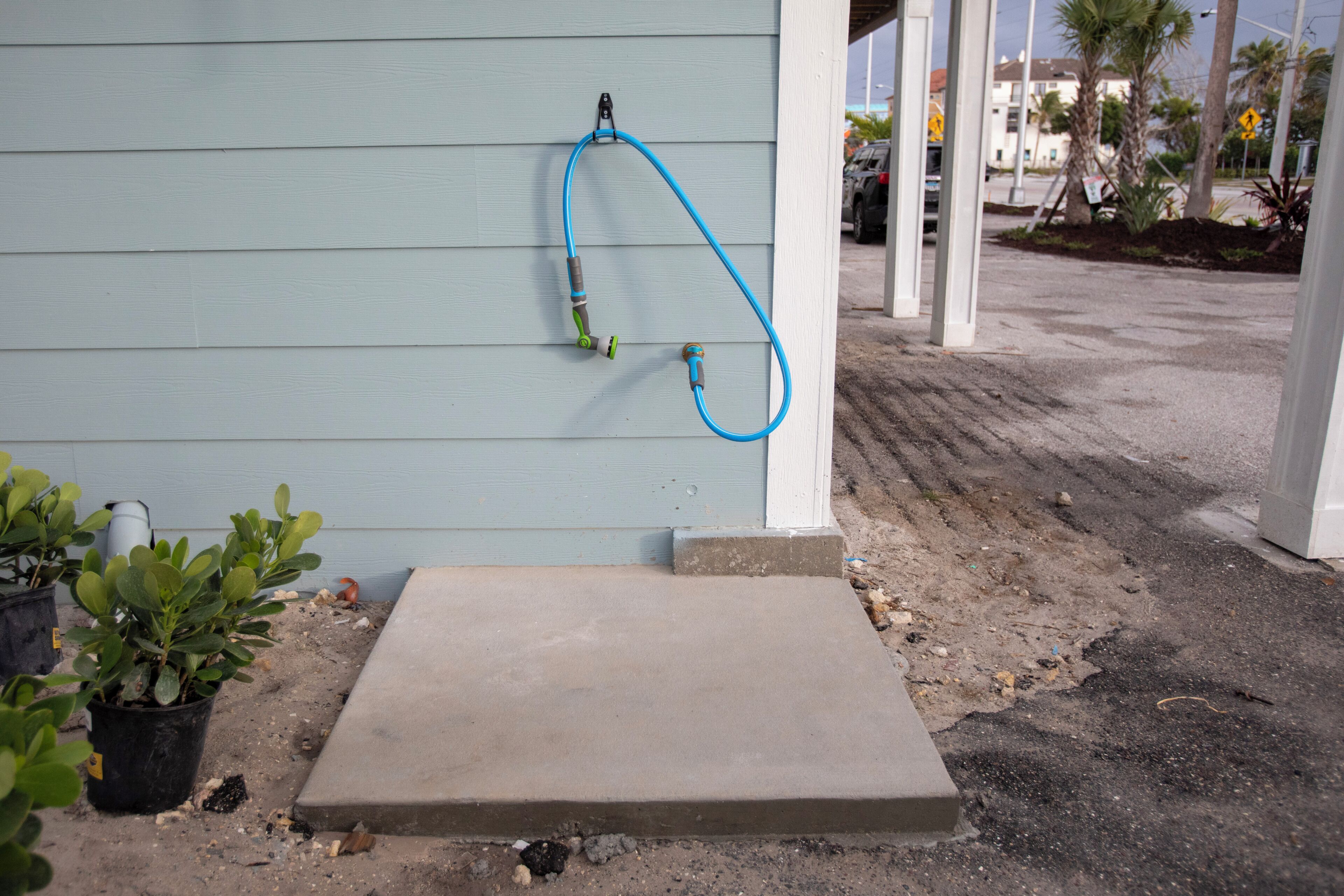 A concrete step leading to a building with a blue exterior wall, a blue hose attached to the wall, and potted plants on the ground.