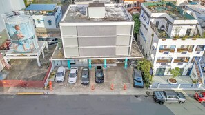 Ein mehrstöckiges Gebäude mit einer zentralen Atriumfläche, einem Parkplatz und anliegenden kleineren Gebäuden.