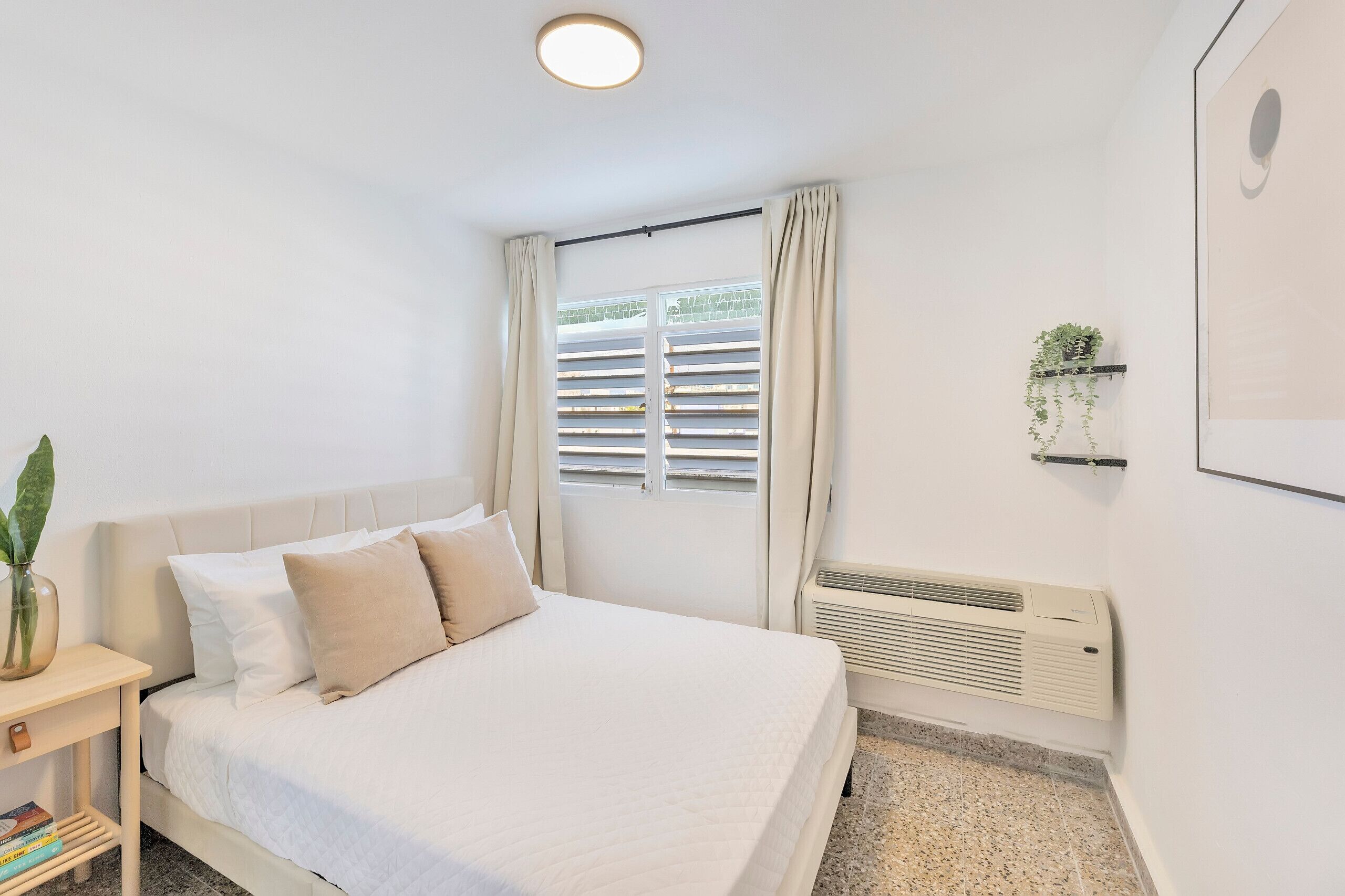 Ein Schlafzimmer mit Bett, Nachttisch und einem Fenster mit Vorhängen.