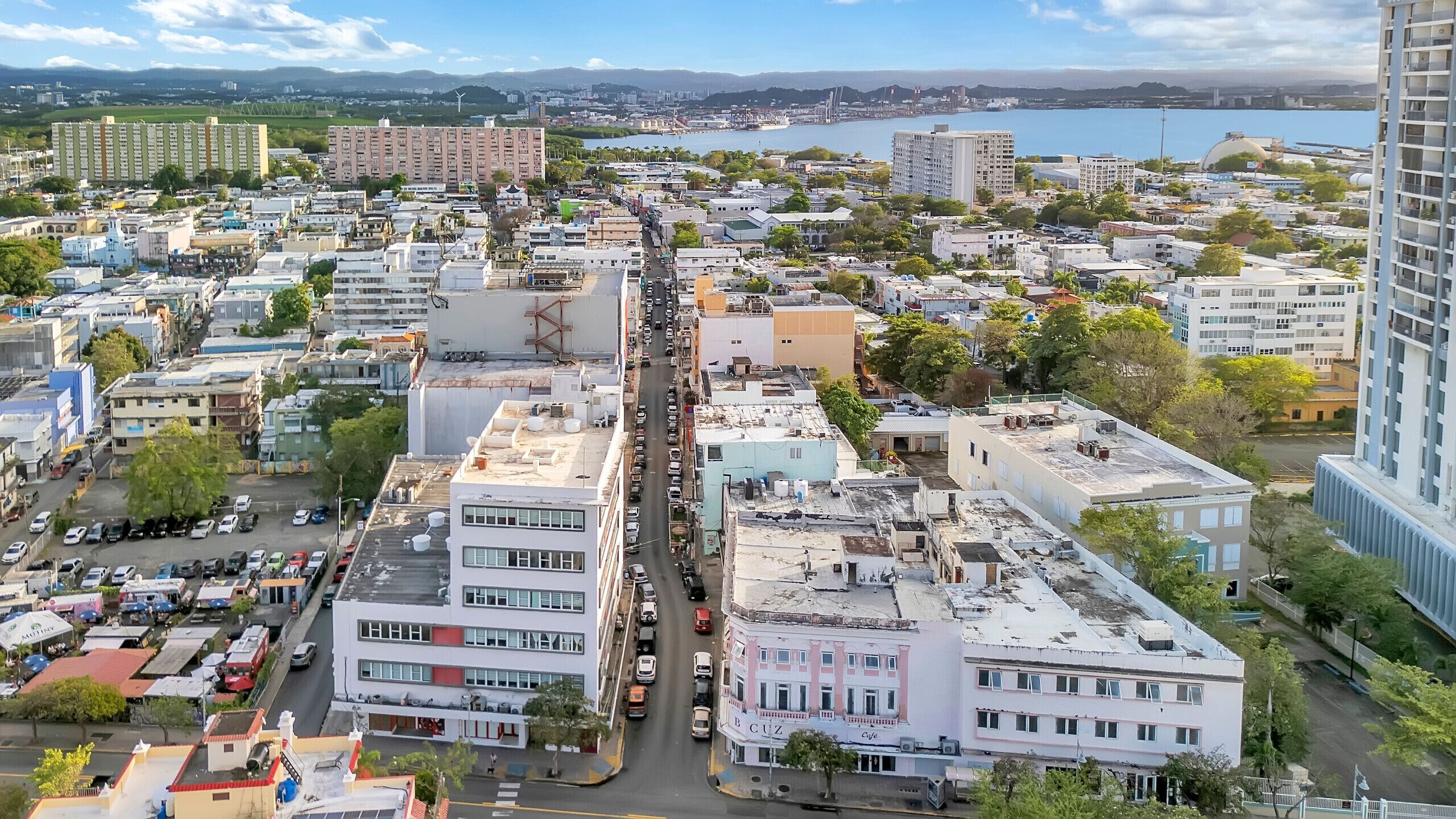 A cityscape with a mix of residential and commercial buildings, a busy street, and a body of water in the background.