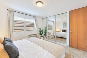Une chambre à coucher comprenant un lit, une porte-fenêtre coulissante, une porte en bois et une fenêtre avec des stores.