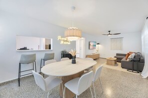 Ein modernes Wohnzimmer mit Essbereich, Deckenventilator und einem großen Fenster mit Vorhängen.