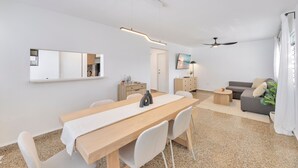 A modern living room with a dining area, a ceiling fan, and a large window with curtains. - Calle Cerra Getaway 3BR w/ Balcony (San Juan)