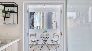A modern kitchen with a built-in sink, a black metal shelf with toiletries, and a view through a glass door to an outdoor seating area with two chairs and a table. - Calle Cerra Getaway 3BR w/ Balcony (San Juan)