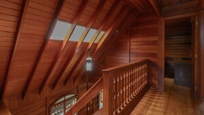 A wooden interior with a sloped ceiling, a balcony with a railing, and a window. - Casa com Lareira e 3 su tes no Parque das Fontes (Campos do Jordão)