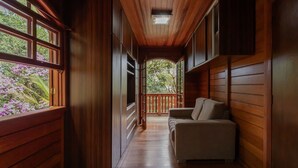 A wooden interior hallway with a sofa, large windows, and a view of greenery outside. - Casa com Lareira e 3 su tes no Parque das Fontes (Campos do Jordão)
