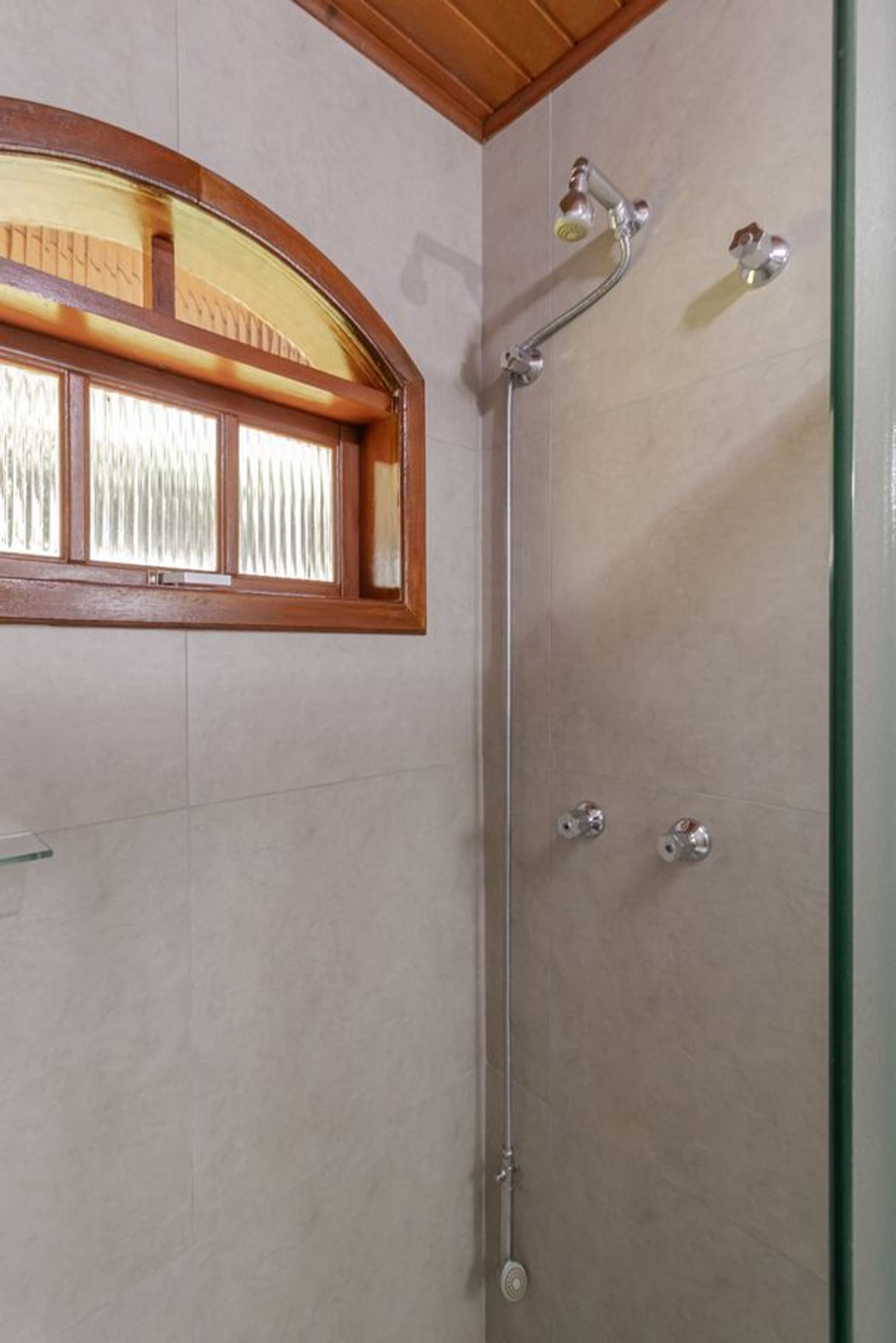 Eine Dusche mit Glastür, Holzfensterrahmen und Duschkopf aus Metall.