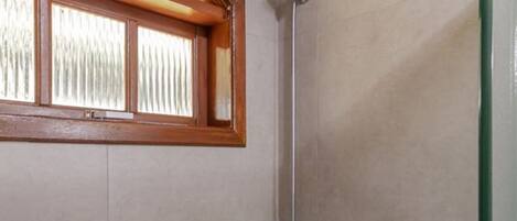Eine Dusche mit Glastür, Holzfensterrahmen und Duschkopf aus Metall.