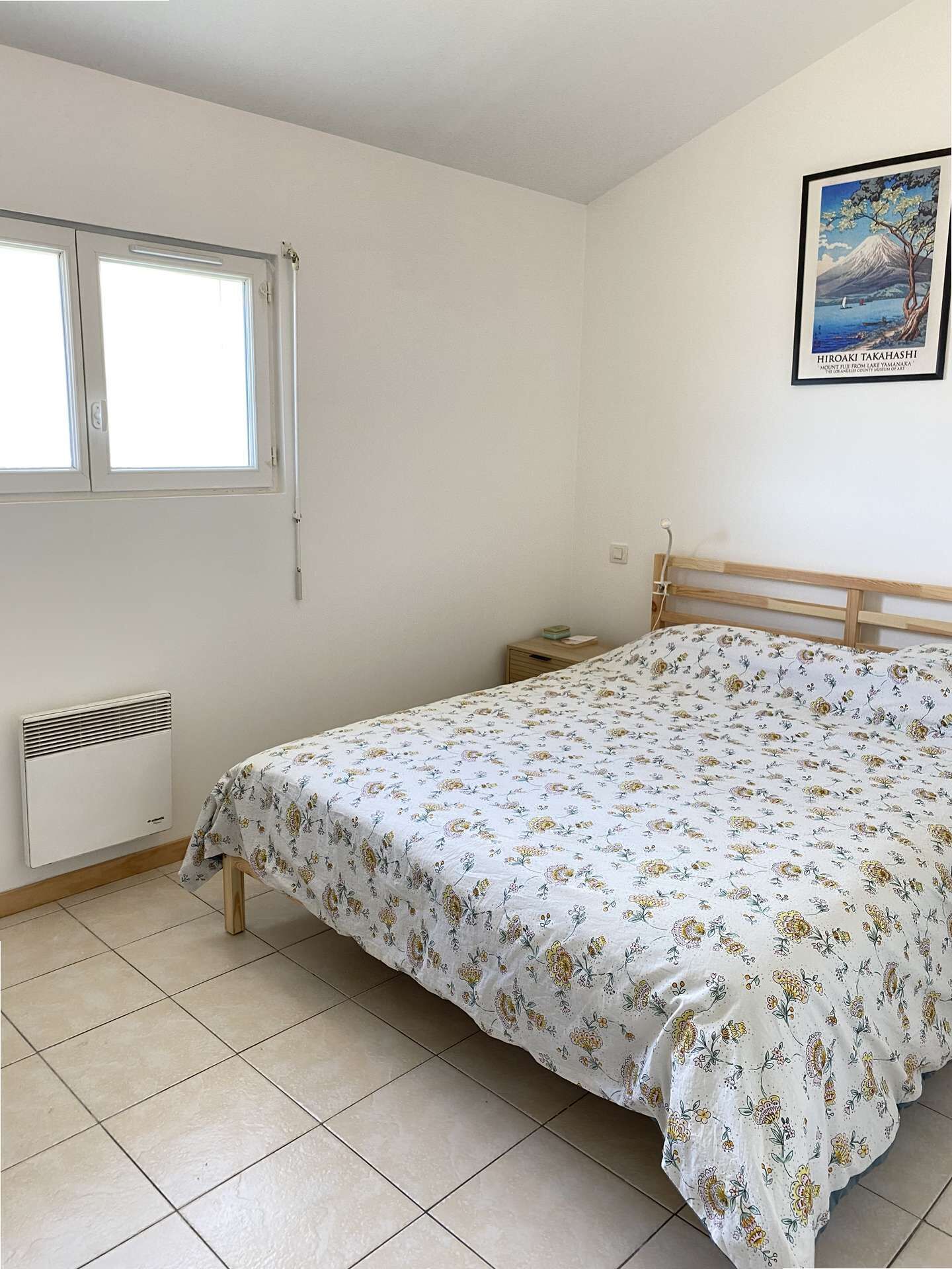 A bedroom with a bed, a radiator, a window, and a wall-mounted picture.