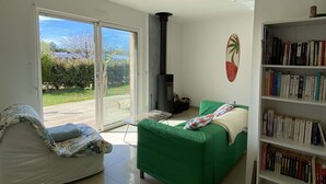 Une pièce avec un canapé vert, un canapé blanc, une bibliothèque, une cheminée et une porte-fenêtre coulissante donnant sur l’extérieur.