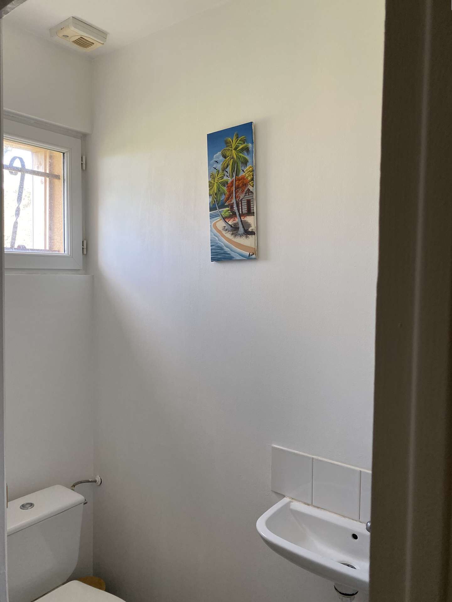 Ein Badezimmer mit Toilette, Waschbecken und einem Bild von einer Strandlandschaft an der Wand.