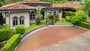 A two-story house with a tiled roof, arched windows, and a landscaped garden with a curved driveway.