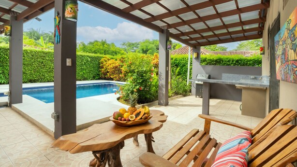 An outdoor patio with a pool, wooden furniture, and a grill area.