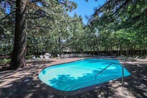 Une piscine entourée d’arbres et de chaises longues, avec une terrasse en bois.