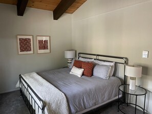 Ein ordentlich eingerichtetes Schlafzimmer mit einem Bett, Nachttischlampen und zwei gerahmten Bildern an der Wand.