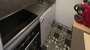 A compact kitchen with a microwave, double cabinets, a sink, and a red coffee maker. - Seignosse océan, 2 bedroom apartment, walking distance to the beach, ideal for a family (SEIGNOSSE)